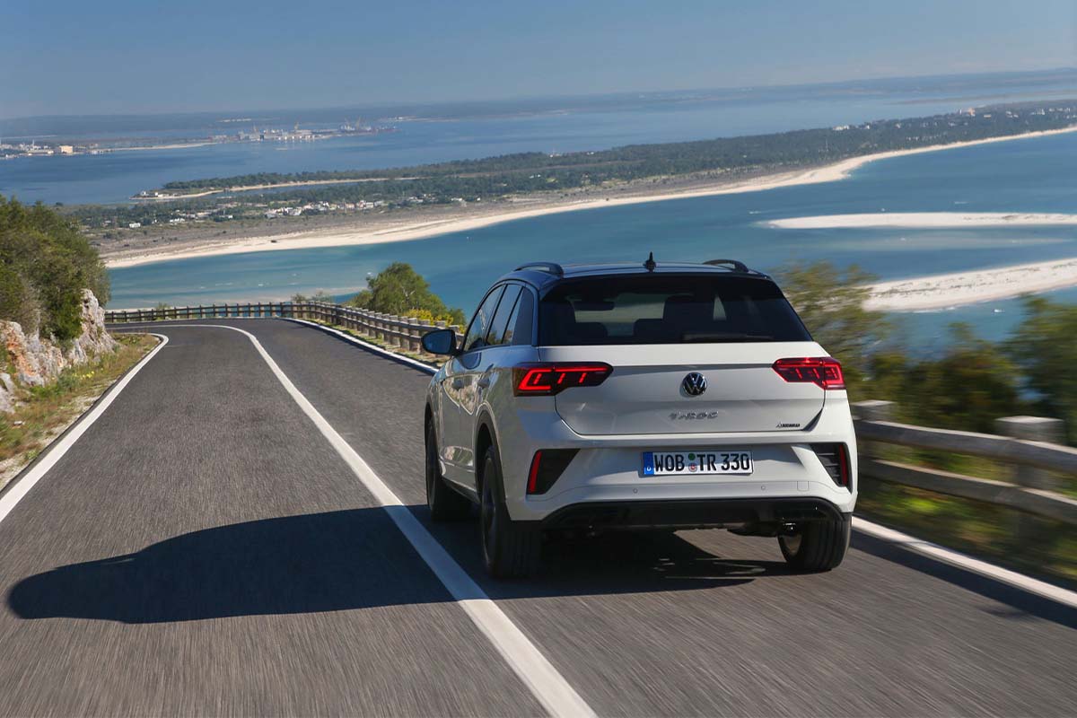 zu sehen ist ein beiger VW T-Roc von hinten auf einer Straße neben dem Meer