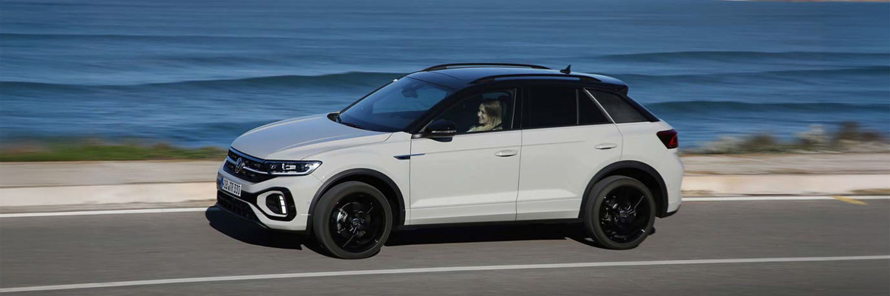 Zu sehen ist ein beiger VW T-Roc von der Seite. Im Hintergrund ist das Meer zu sehen.