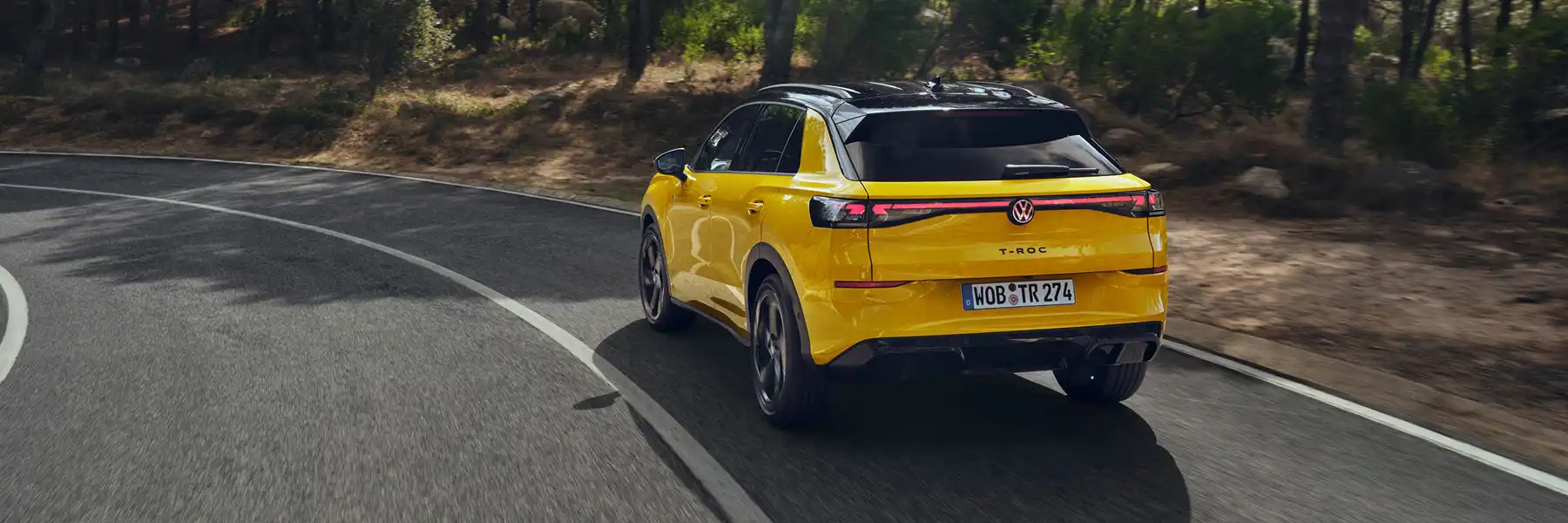 Zu sehen ist ein gelber VW T-Roc Live von hinten auf einer Landstraße